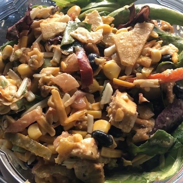 A close-up of a breakfast salad with corn, black beans, cheese, and tortilla strips.
