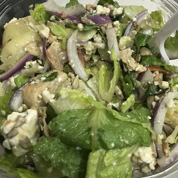 Close-up of a salad with lettuce, red onion, artichoke hearts, feta cheese, and sunflower seeds.
