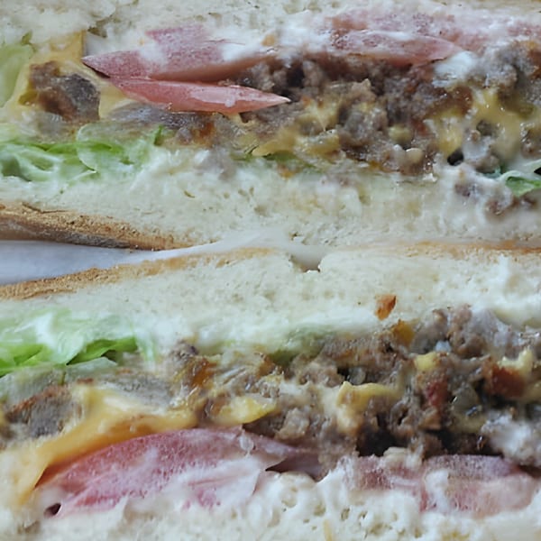 Close-up of a breakfast sandwich cut in half, revealing sausage, cheese, lettuce, and tomato.