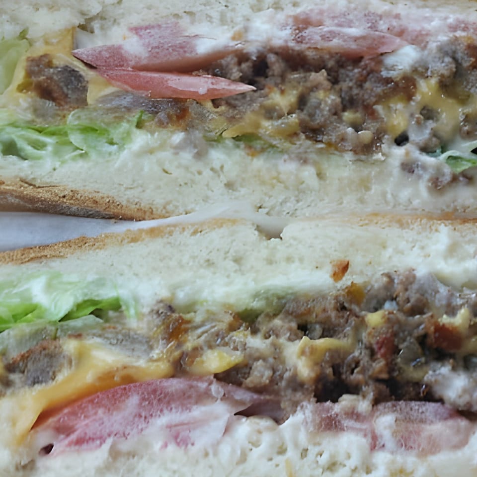 Close-up of a breakfast sandwich cut in half, revealing sausage, cheese, lettuce, and tomato.