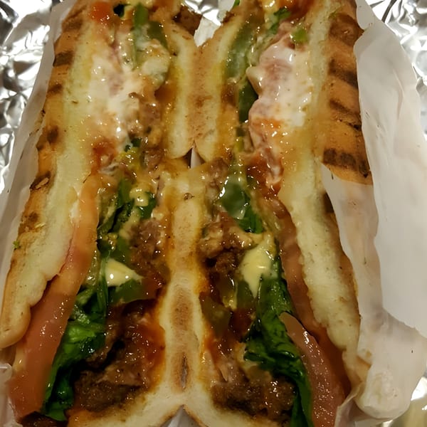 A Tasty Picks breakfast sandwich, cut in half, revealing meat, lettuce, tomato, and sauce.
