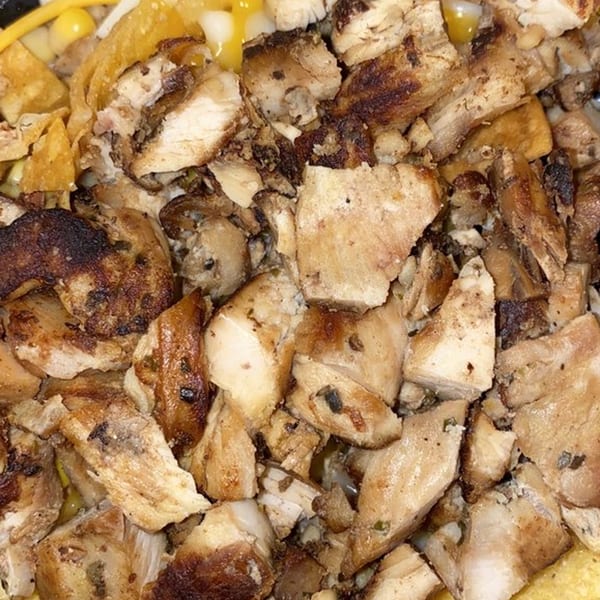Close-up of diced, grilled chicken pieces with some corn and tortilla chips visible.