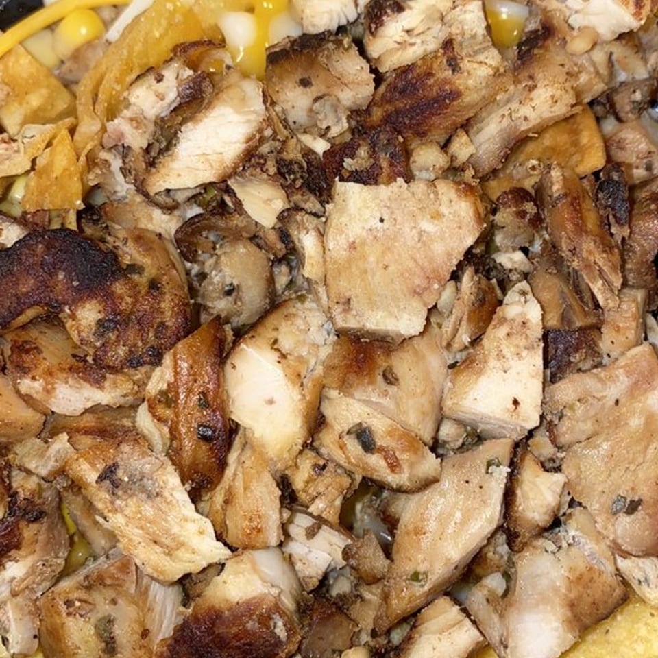 Close-up of diced, grilled chicken pieces with some corn and tortilla chips visible.