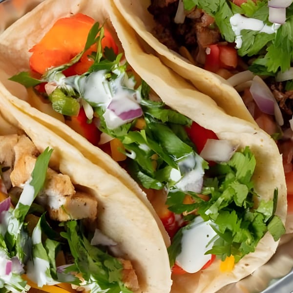 Three breakfast tacos filled with various meats, vegetables, and a creamy white sauce.